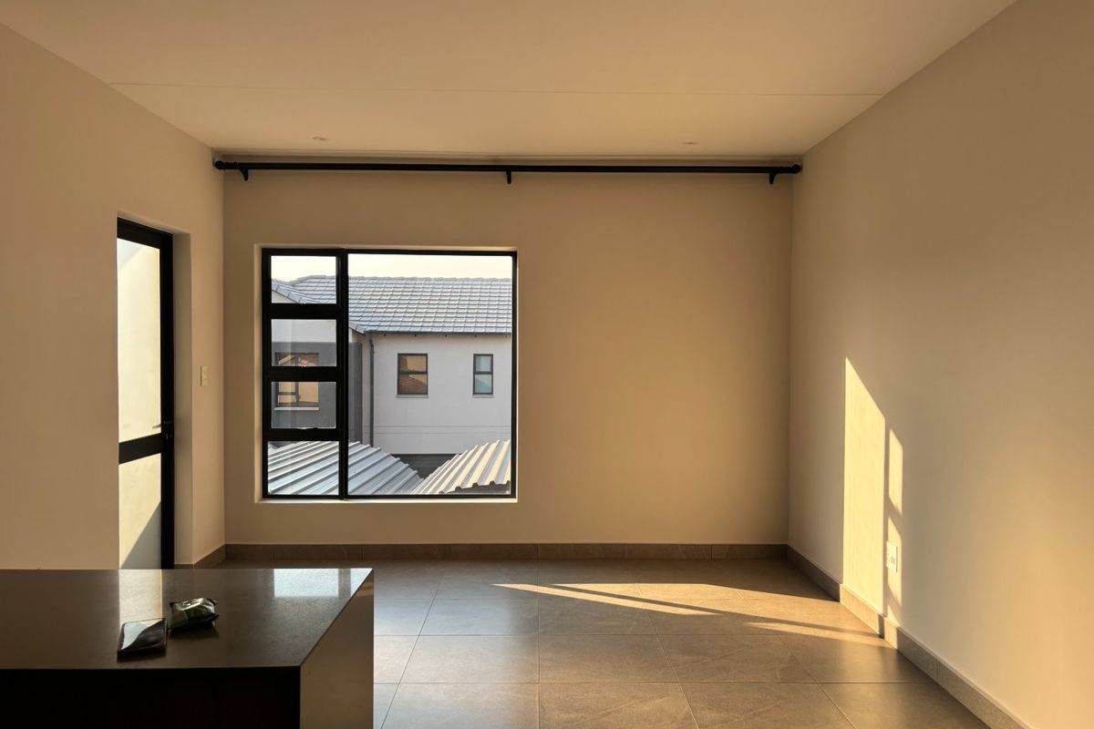 A bright, empty living area featuring neutral tiled flooring, modern aluminium window frames, and recessed downlighting, offering a clean canvas for interior design.