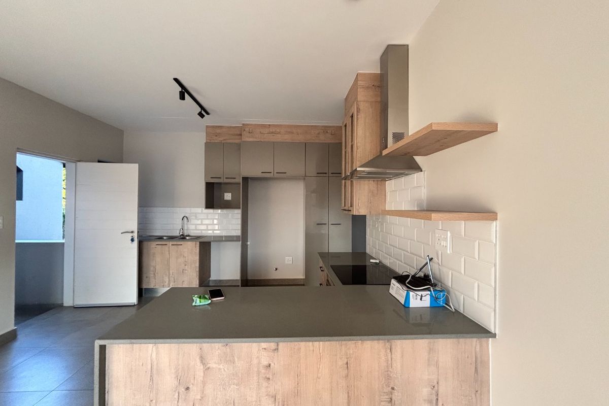 Modern kitchen featuring wood-look cabinetry, stone countertops, subway tile backsplash, integrated hob, and extractor fan in an open-plan layout.