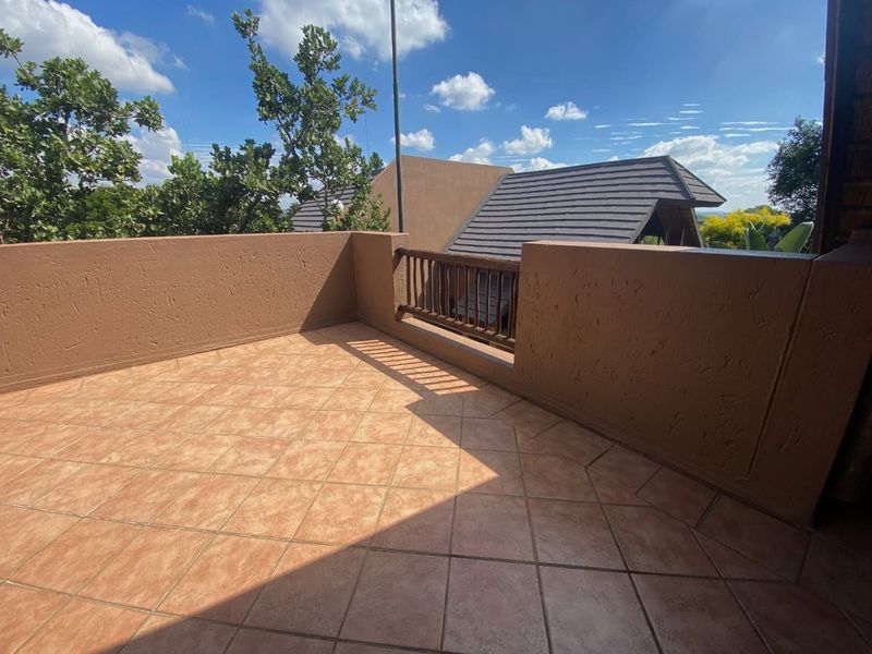 An open-air balcony featuring tiled flooring and a masonry balustrade with timber railing, offering elevated views of the surrounding area.