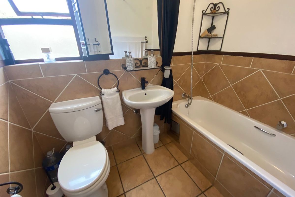 A functional bathroom featuring a pedestal basin, toilet, and bathtub with a handheld shower mixer, finished with neutral-toned wall and floor tiles.