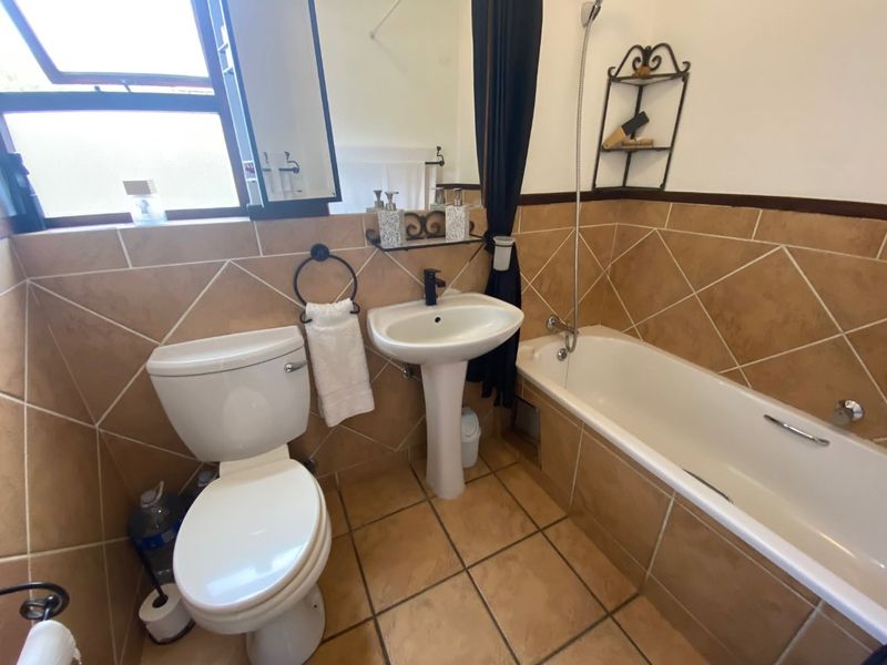 A functional bathroom featuring a pedestal basin, toilet, and bathtub with a handheld shower mixer, finished with neutral-toned wall and floor tiles.