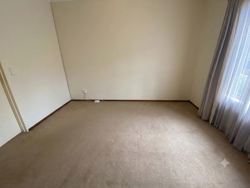 A clean, empty bedroom featuring neutral wall paint, carpeted flooring, and existing curtain tracks, providing a blank canvas for personalization.