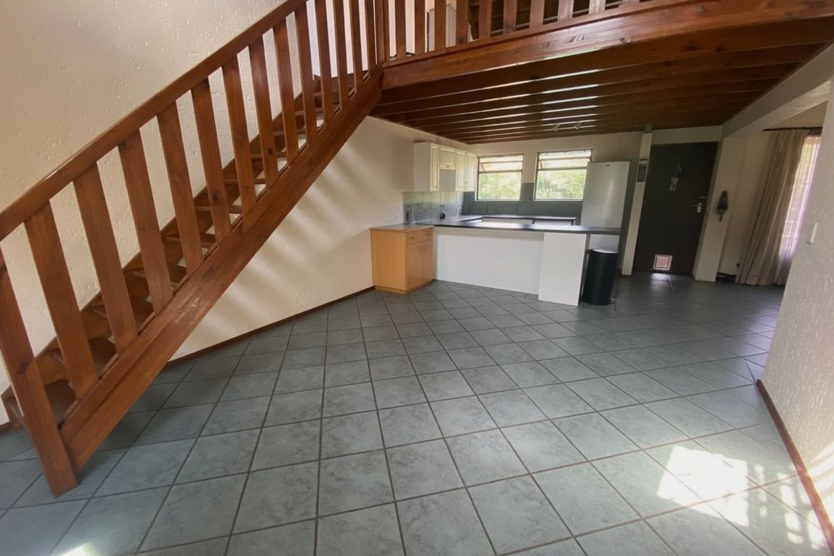 Open-plan living area featuring a wooden staircase leading to a mezzanine level, tiled flooring, and a functional kitchen space.