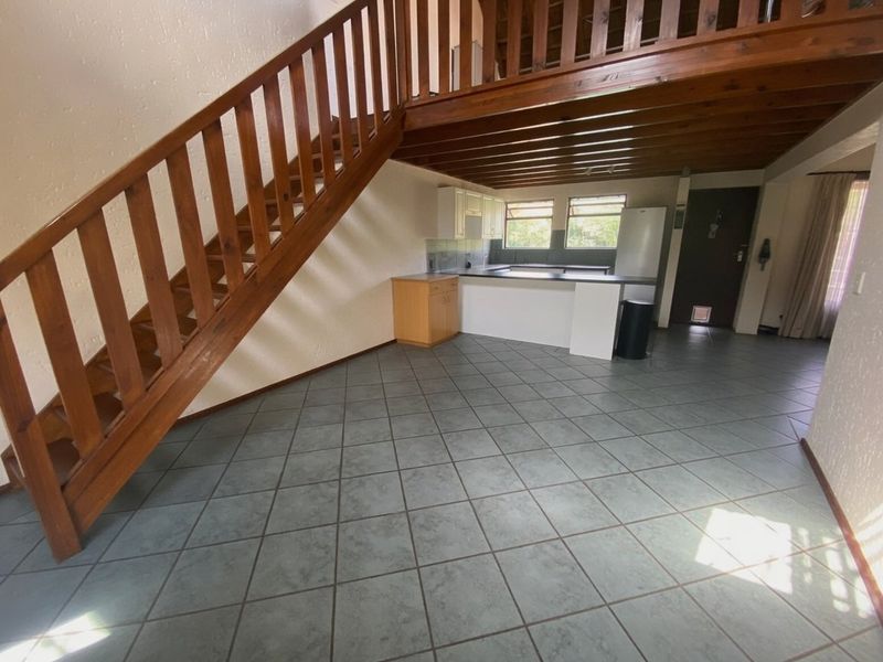 Open-plan living area featuring a wooden staircase leading to a mezzanine level, tiled flooring, and a functional kitchen space.