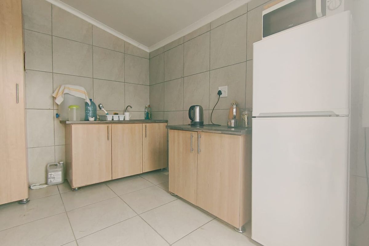 A functional kitchen area featuring light wood-finish cabinetry, tiled walls and flooring, and a compact layout suitable for a commercial or office kitchenette.