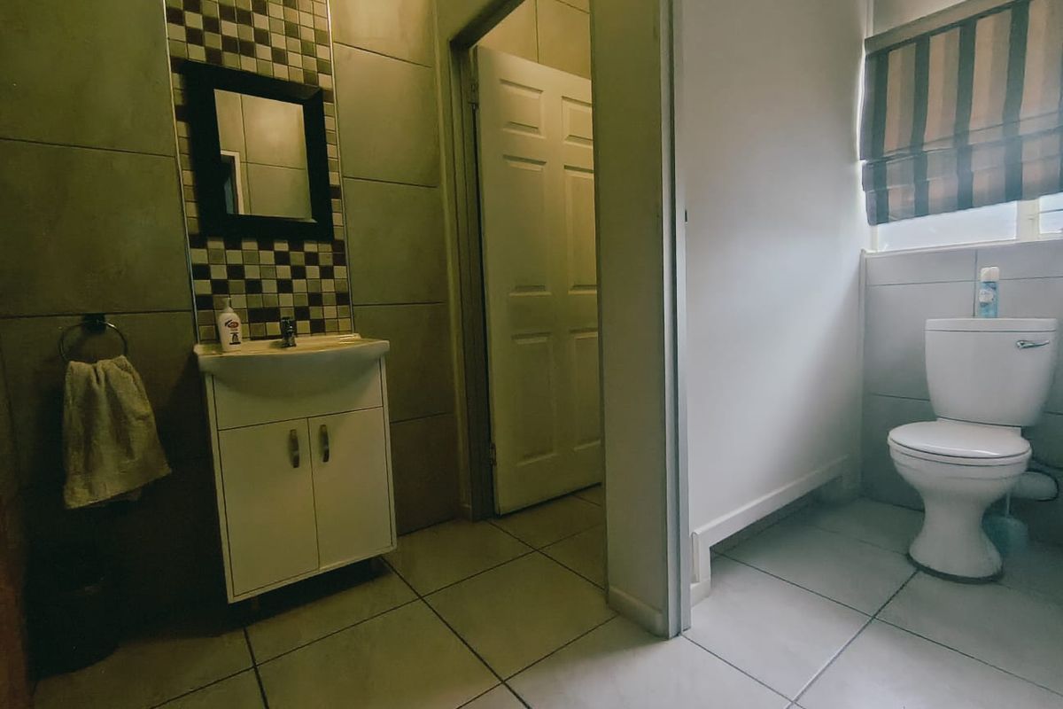 A functional bathroom featuring a vanity cabinet with basin, tiled walls with decorative accents, and a separate toilet area.