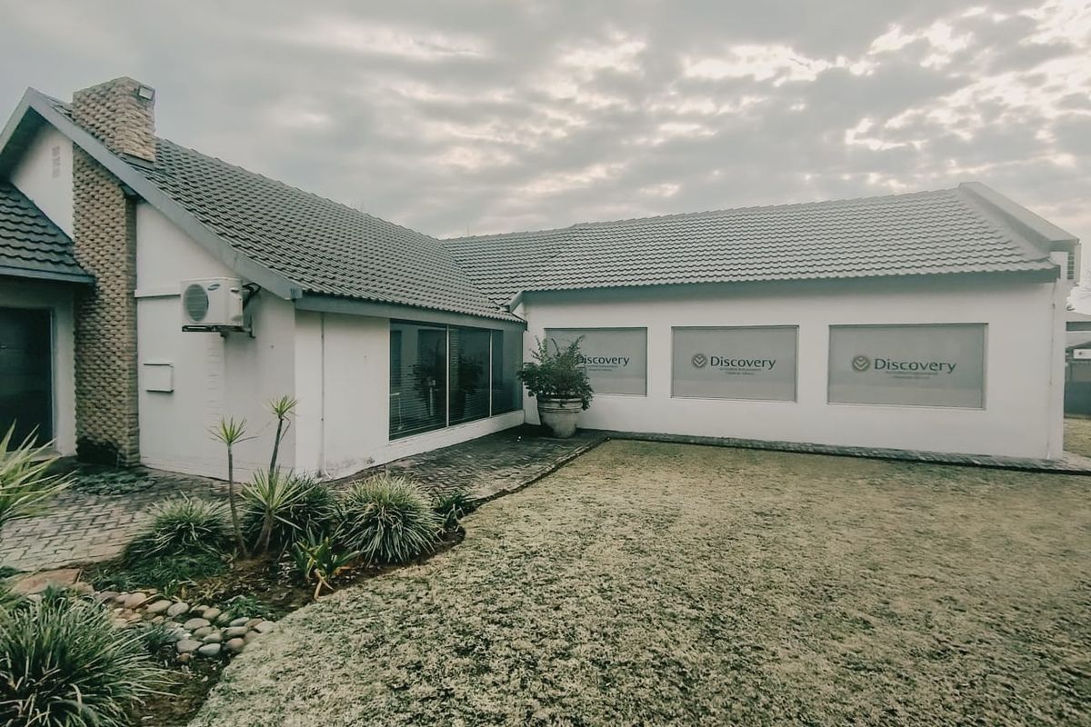 Rear view of a commercial property featuring a tiled roof, paved patio area, and a lawn, with branded window signage.
