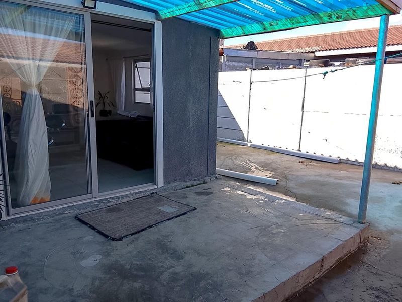 A covered concrete patio area featuring a sliding glass door entrance and a corrugated plastic roof structure.