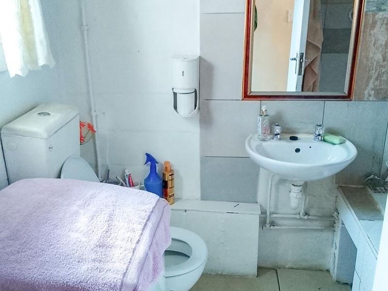 A compact bathroom featuring a wall-mounted basin, ceramic toilet, and tiled splashback, requiring cosmetic updates to improve its overall condition and aesthetic appeal.