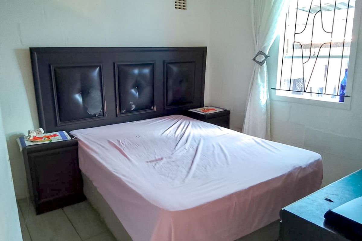 A bedroom featuring tiled flooring and a window fitted with security bars.