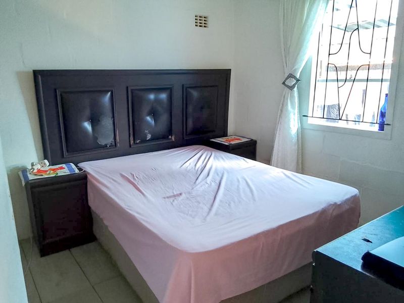 A bedroom featuring tiled flooring and a window fitted with security bars.