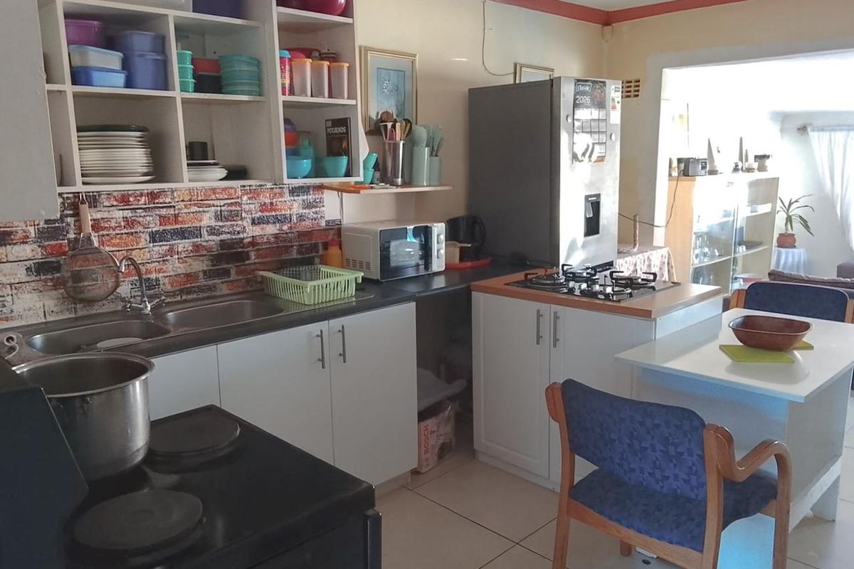 A functional kitchen featuring white cabinetry, a gas hob, stainless steel sink, and brick-effect splashback tiling, offering a practical layout for daily meal preparation.