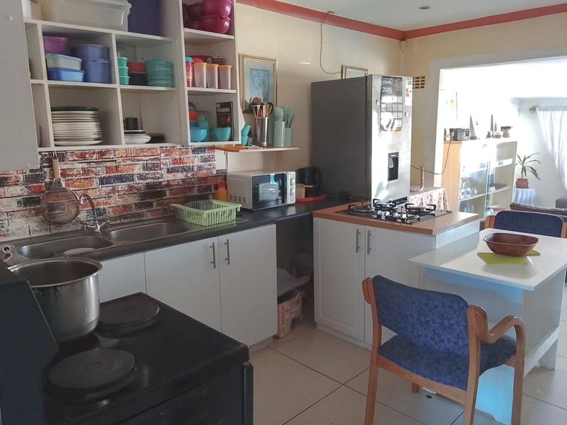 A functional kitchen featuring white cabinetry, a gas hob, stainless steel sink, and brick-effect splashback tiling, offering a practical layout for daily meal preparation.