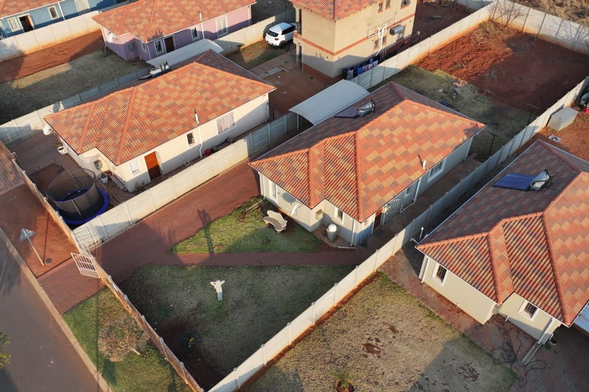 Aerial view of a residential property featuring a tiled roof house, paved driveway, carport, and enclosed garden with precast concrete boundary walls.