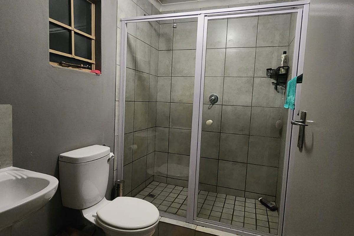 A functional bathroom featuring a shower enclosure, pedestal basin, and toilet with neutral wall and floor tiling.