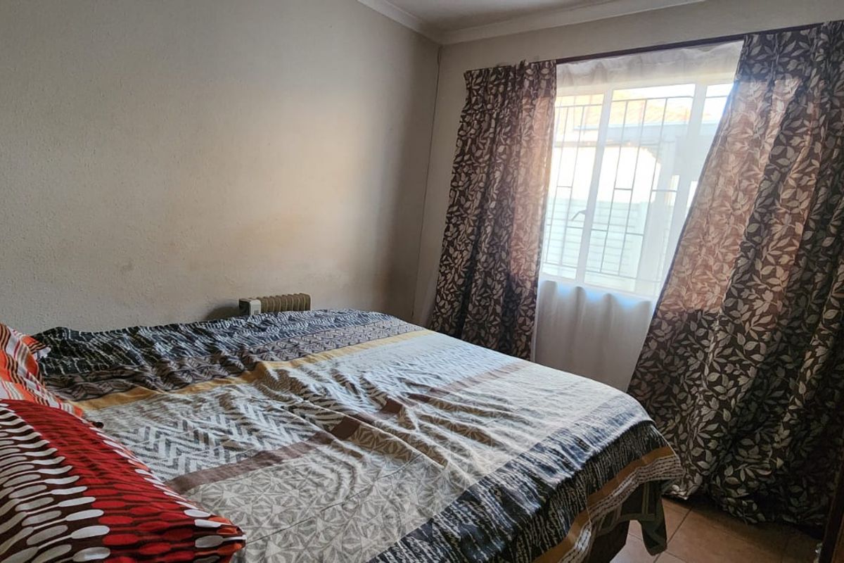 A standard bedroom featuring a window with security bars and a built-in cupboard, providing functional storage space.