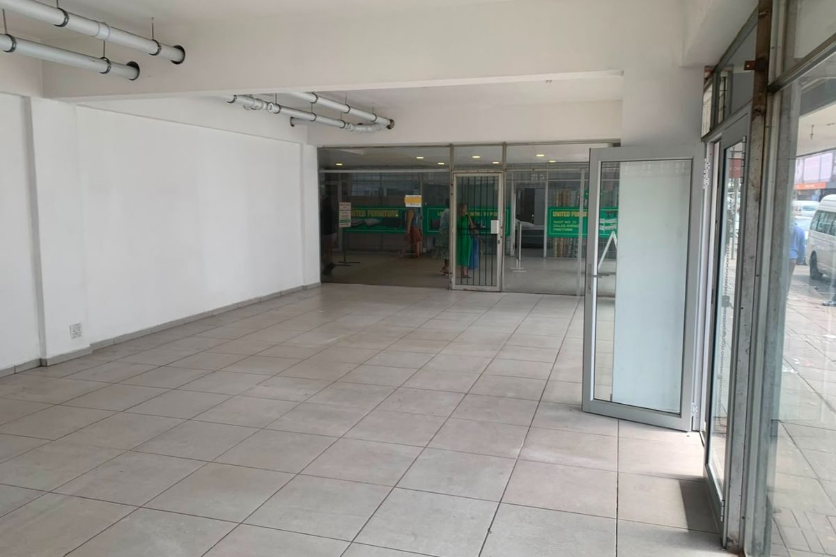 A vacant commercial entry space featuring tiled flooring, exposed ceiling piping, and large glass storefront doors providing street-level visibility.