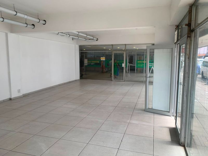 A vacant commercial entry space featuring tiled flooring, exposed ceiling piping, and large glass storefront doors providing street-level visibility.