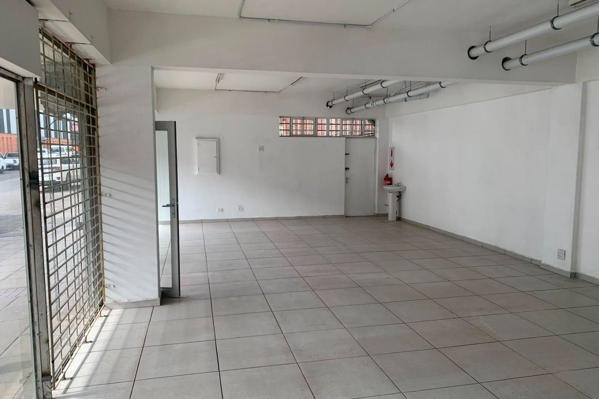 An open-plan commercial space featuring tiled flooring, exposed ceiling services, and a wall-mounted basin, suitable for various business or retail applications.