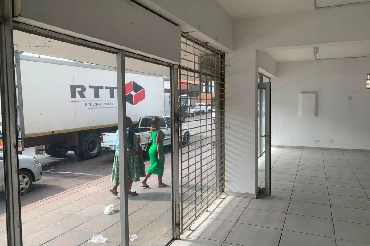 Empty commercial entry space featuring tiled flooring, a secure metal gate, and large glass storefront windows facing the street.