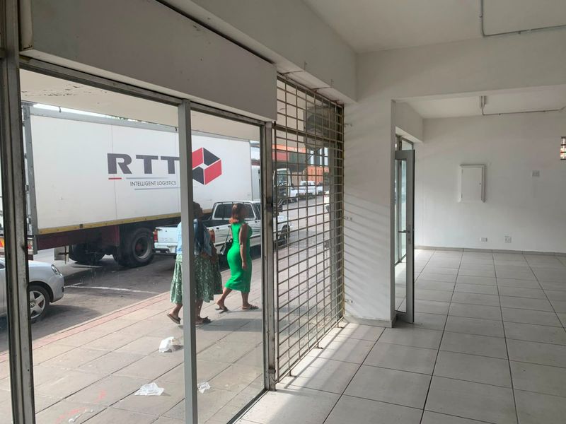 Empty commercial entry space featuring tiled flooring, a secure metal gate, and large glass storefront windows facing the street.
