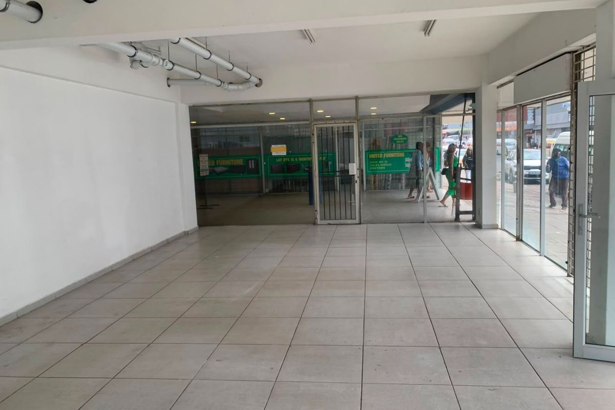 An open-plan commercial retail space featuring tiled flooring, a large glass storefront, and exposed ceiling infrastructure, suitable for various business applications.