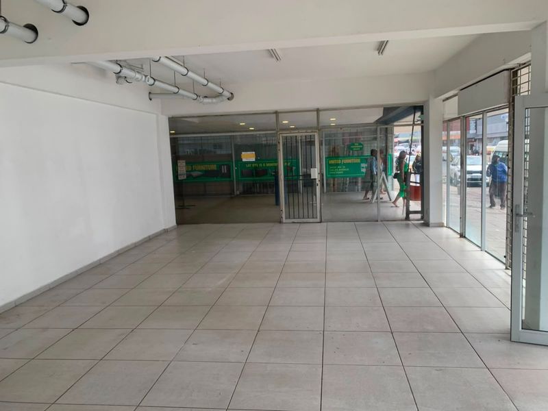 An open-plan commercial retail space featuring tiled flooring, a large glass storefront, and exposed ceiling infrastructure, suitable for various business applications.