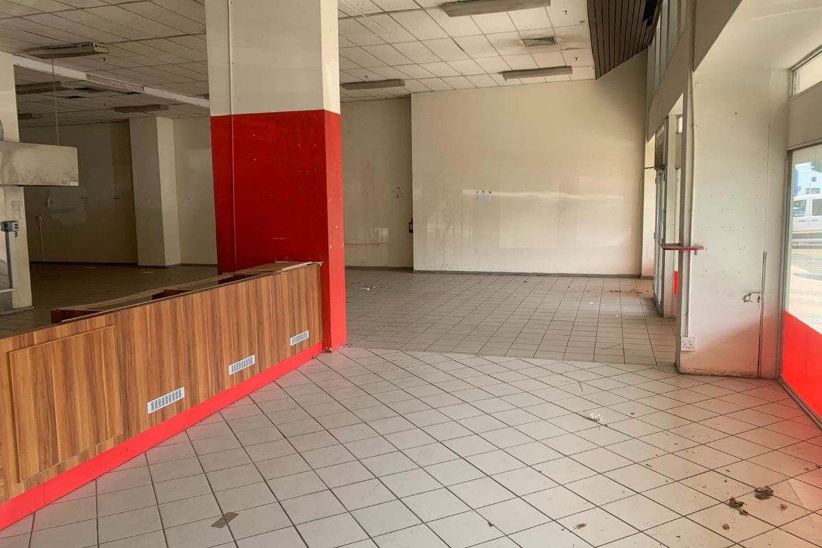 Vacant commercial open-plan space featuring ceramic floor tiles, a built-in service counter, and large glass storefront windows, requiring refurbishment.