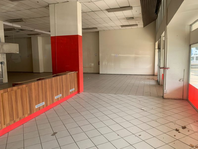 Vacant commercial open-plan space featuring ceramic floor tiles, a built-in service counter, and large glass storefront windows, requiring refurbishment.