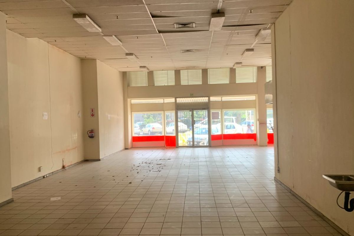 Vacant commercial open-plan space featuring tiled flooring, a suspended ceiling, and a glass storefront entrance, suitable for retail or office use.