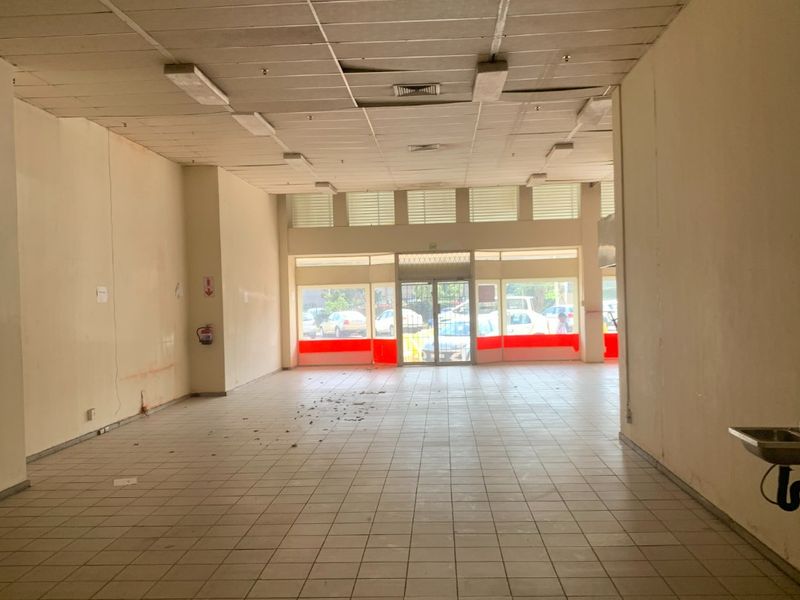 Vacant commercial open-plan space featuring tiled flooring, a suspended ceiling, and a glass storefront entrance, suitable for retail or office use.