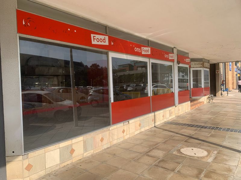 Commercial storefront featuring large glass display windows, a covered pedestrian walkway, and tiled facade detailing, suitable for retail or food service operations.