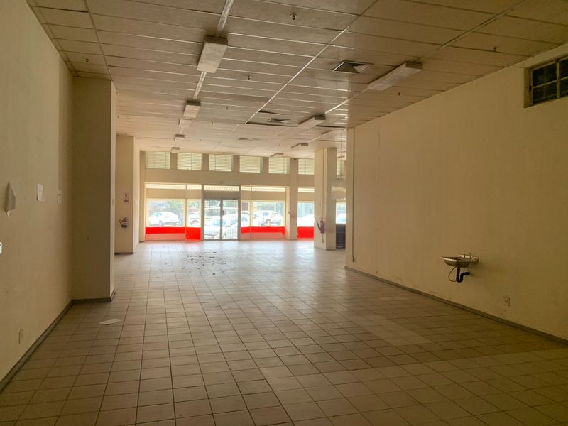 A vacant open-plan commercial space featuring tiled flooring, a suspended ceiling with integrated lighting, and large storefront windows providing natural light.