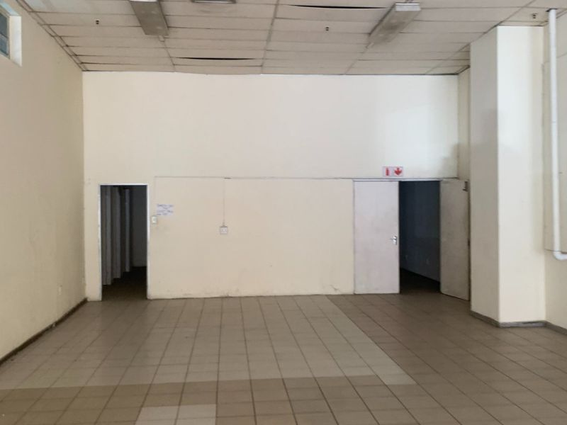 A vacant, open-plan commercial space featuring ceramic tiled flooring, a suspended ceiling with integrated lighting, and multiple access points.