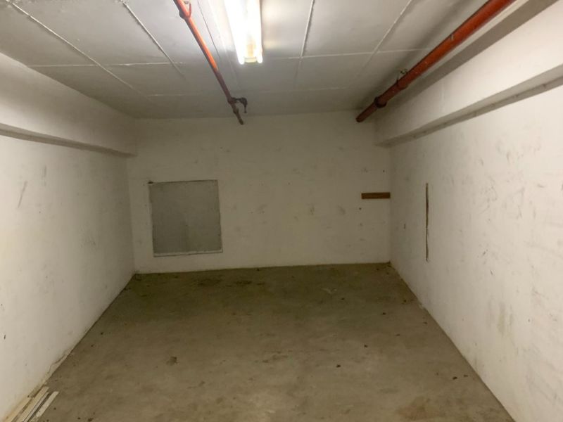 An empty utility or storage space featuring exposed fire sprinkler pipes, concrete flooring, and basic fluorescent lighting.