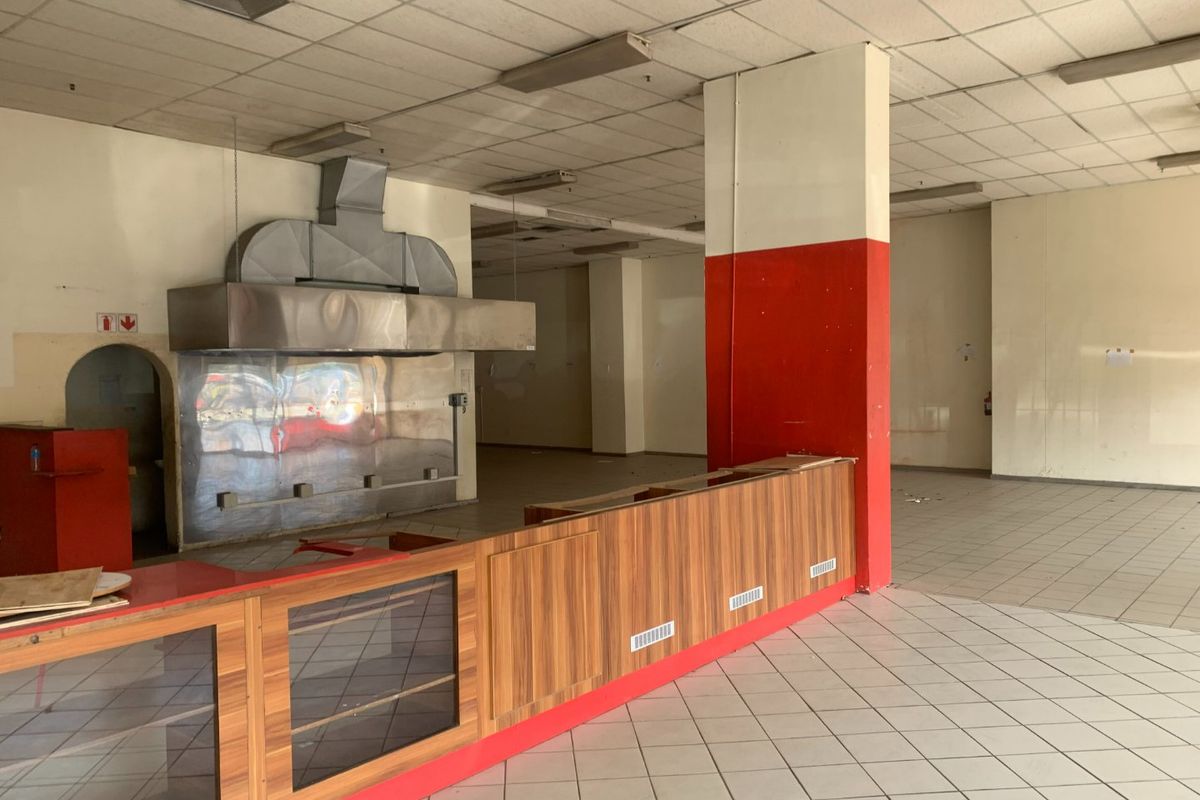 Vacant commercial kitchen space featuring a large stainless steel extractor hood, built-in service counter, tiled flooring, and suspended ceiling grid.