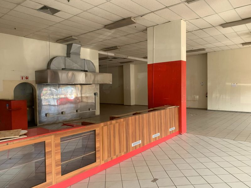 Vacant commercial kitchen space featuring a large stainless steel extractor hood, built-in service counter, tiled flooring, and suspended ceiling grid.