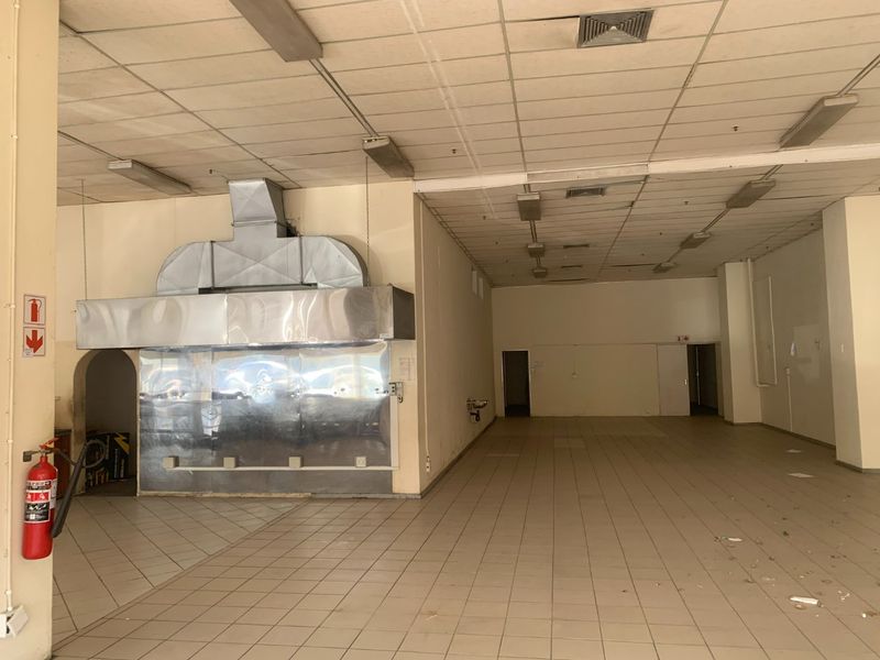 A vacant commercial kitchen space featuring a large stainless steel extractor hood, tiled flooring, and suspended ceiling, suitable for restaurant or food service operations.