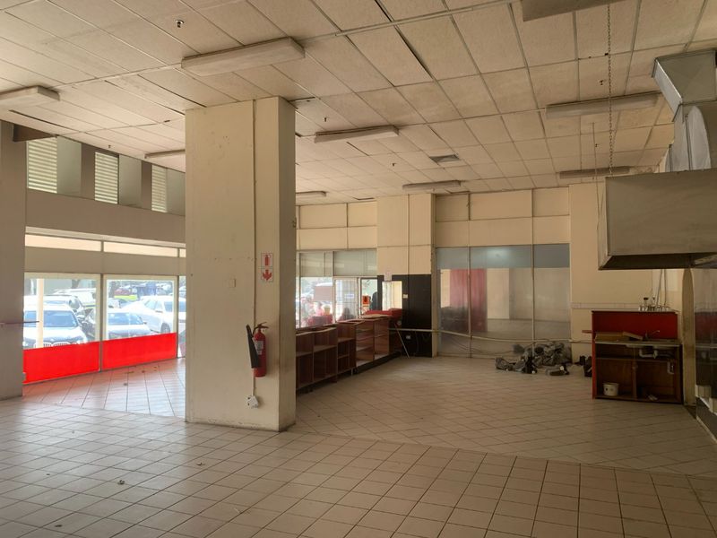 Spacious open-plan commercial unit featuring ceramic tiled flooring, suspended ceilings, built-in service counter, and a stainless steel extractor hood, suitable for retail or food service.