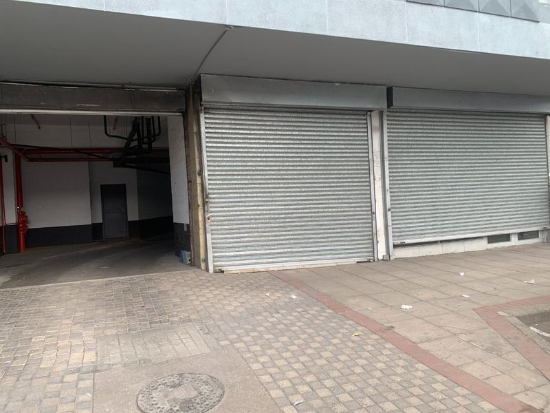 Commercial storefront exterior featuring metal roller shutters and adjacent access to a covered parking or utility area.