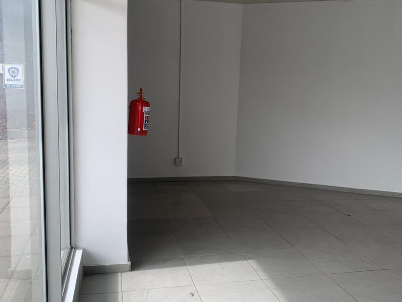 An empty commercial office space featuring large glass windows, tiled flooring, and a suspended ceiling with integrated lighting.
