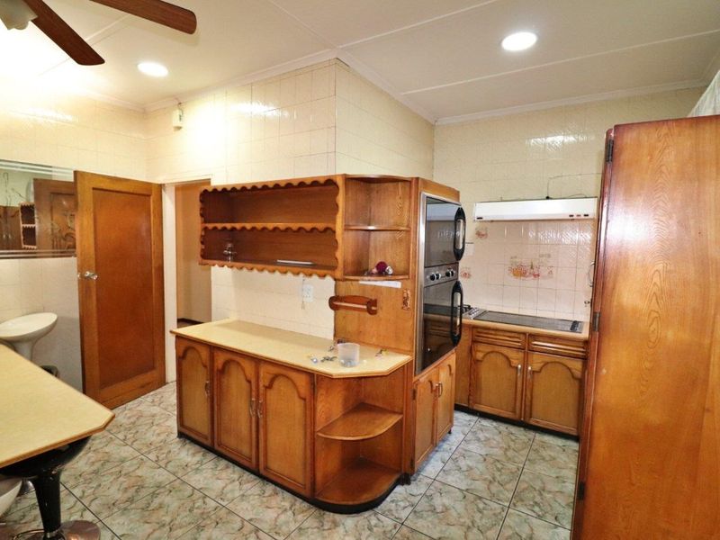 A functional kitchen featuring dated wooden cabinetry, built-in double oven, electric hob, and tiled finishes throughout.