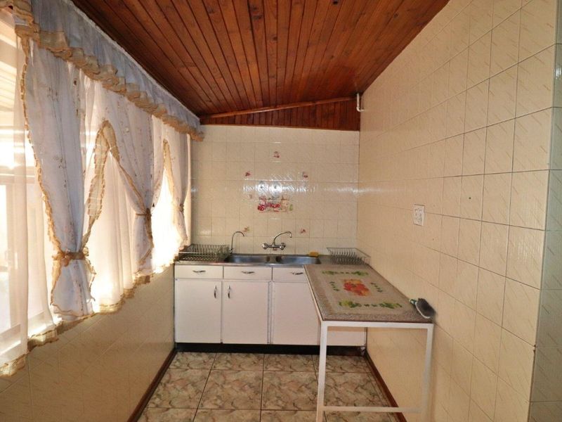 A functional scullery area featuring a double sink, tiled walls, and a timber-clad ceiling, offering a practical space for food preparation and wash-up.