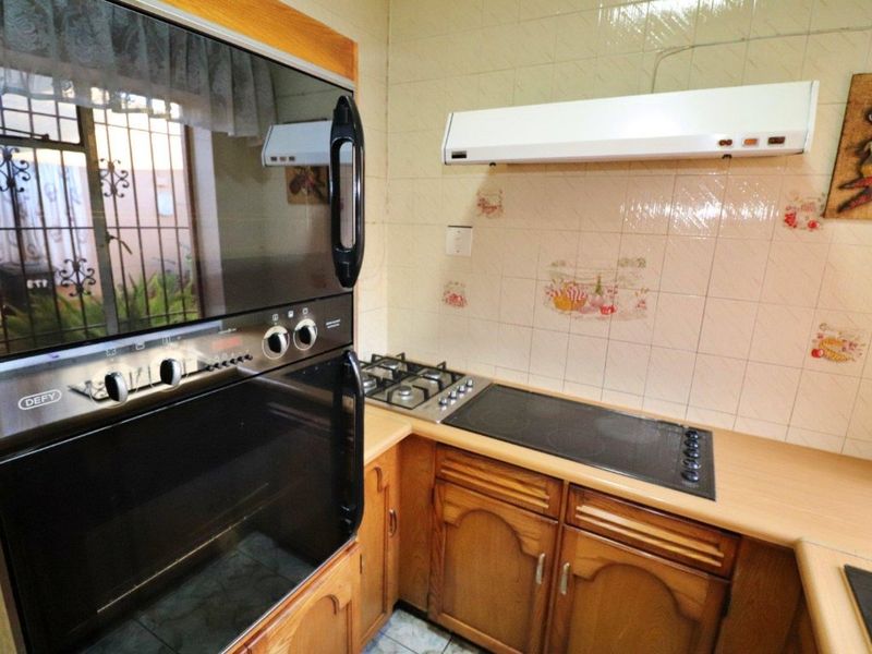A functional kitchen featuring wooden cabinetry, a built-in oven, and a combination of gas and electric hobs with a tiled backsplash.