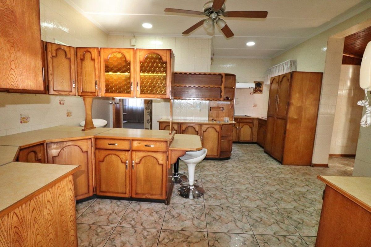 A spacious kitchen featuring extensive built-in wooden cabinetry, tiled flooring, and a ceiling fan, offering a functional layout with significant potential for modern updates.