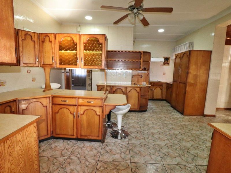 A spacious kitchen featuring extensive built-in wooden cabinetry, tiled flooring, and a ceiling fan, offering a functional layout with significant potential for modern updates.