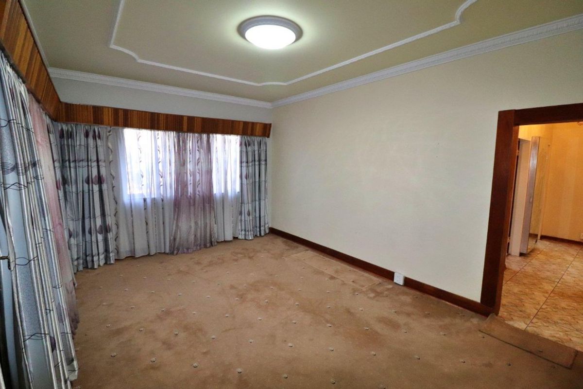 A spacious, empty bedroom featuring carpeted flooring, decorative ceiling cornices, and a wooden curtain pelmet, leading into an adjacent tiled area.