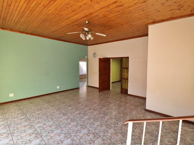 Spacious living area featuring a timber tongue and groove ceiling, ceiling fan, and ceramic tiled flooring, offering a blank canvas for renovation.