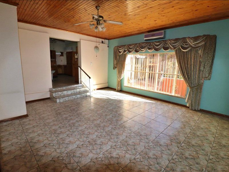 Spacious living area featuring timber ceiling, ceramic tiled flooring, split system air conditioning, and large window with security bars.