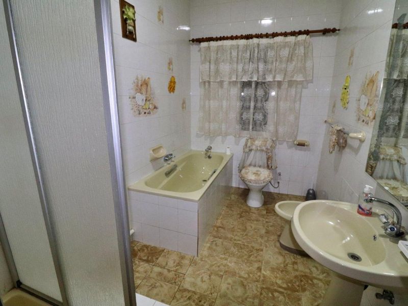 A dated bathroom featuring a built-in bathtub, pedestal sink, bidet, and toilet with tiled finishes throughout.